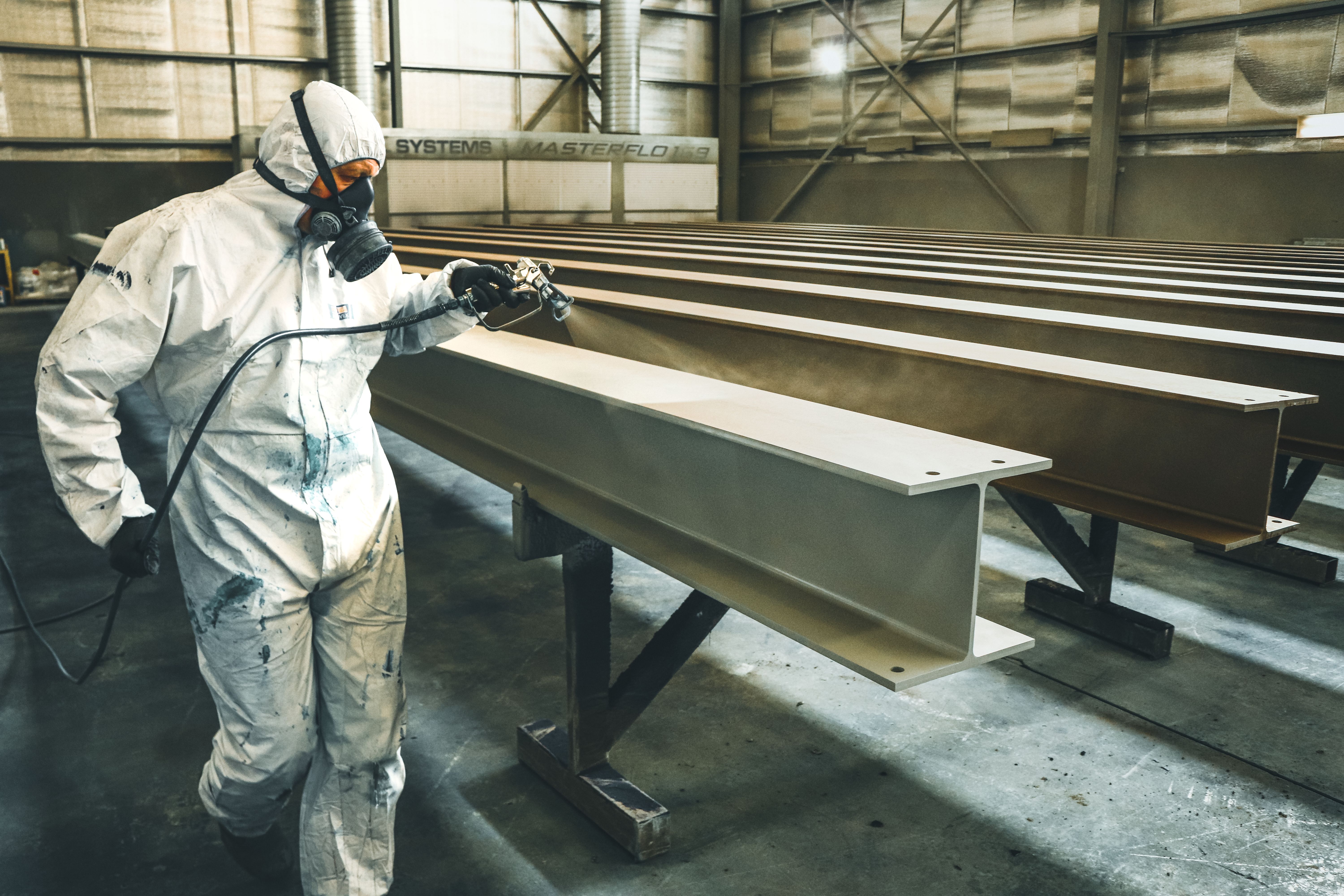 Worker applying an architectural coating to an unfinished metal beam